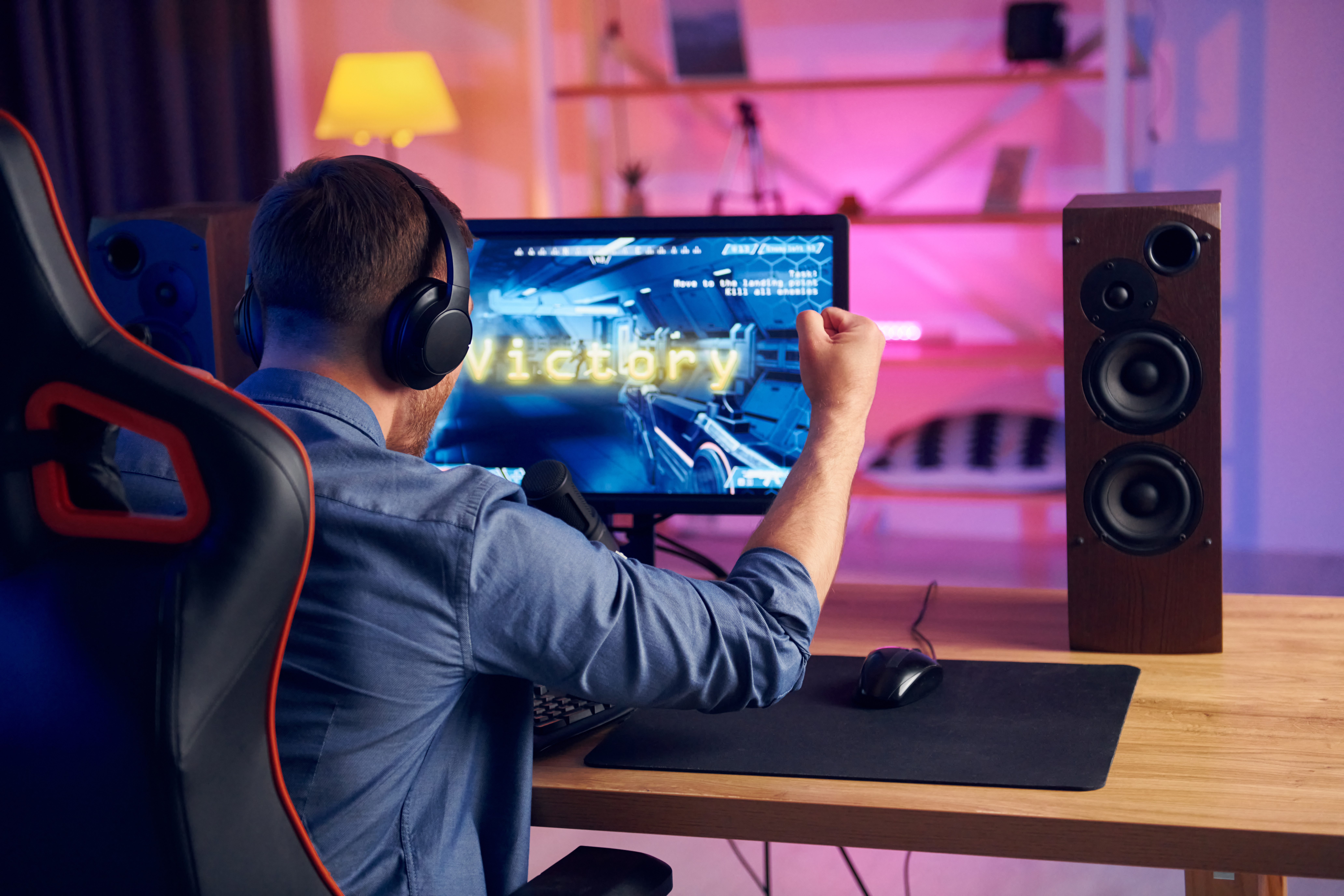View from behind. Online streamer playing FPS shooter game at home.